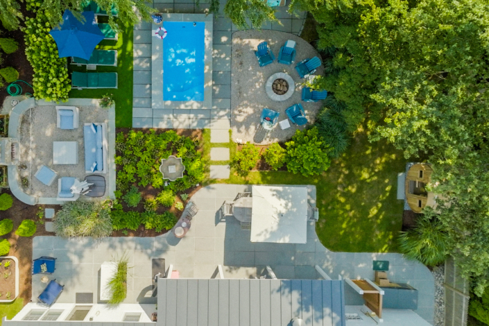 Drone view of a landscaped backyard with a bluestone patio, sauna, bluestone stepping stones connecting to a bluestone-lined plunge pool, and new sod lawn.