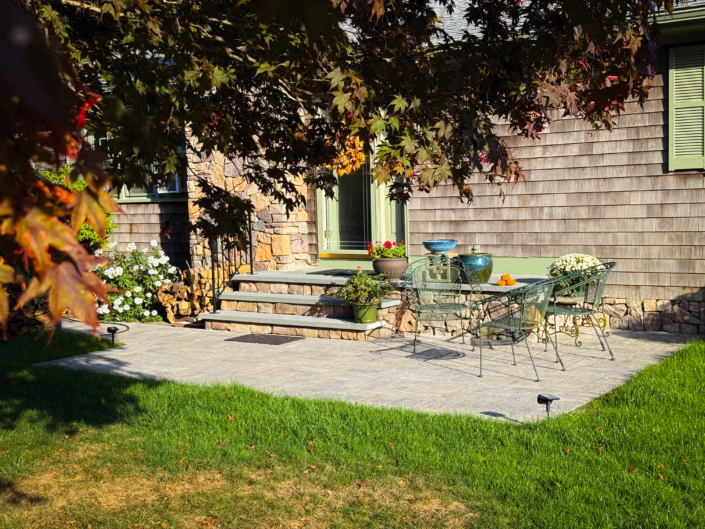 Front steps with thermal bluestone caps and veneer stone faces leading to a small paver patio, with fall leaves in the foreground.