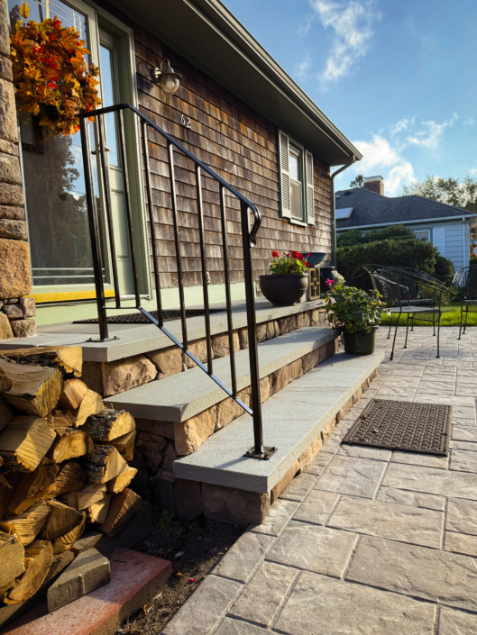 Front steps capped with thermal bluestone faced with veneer stones leading to a paver patio.