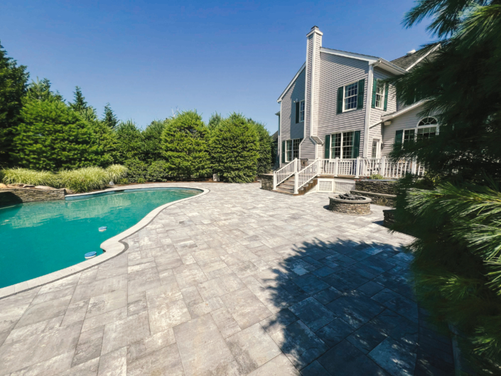Paver patio surrounding an in-ground swimming pool with natural stone features in the summer.