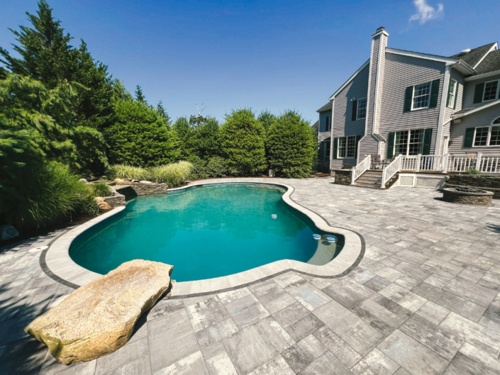 Paver patio surrounding an in-ground swimming pool with natural stone features in the summer.