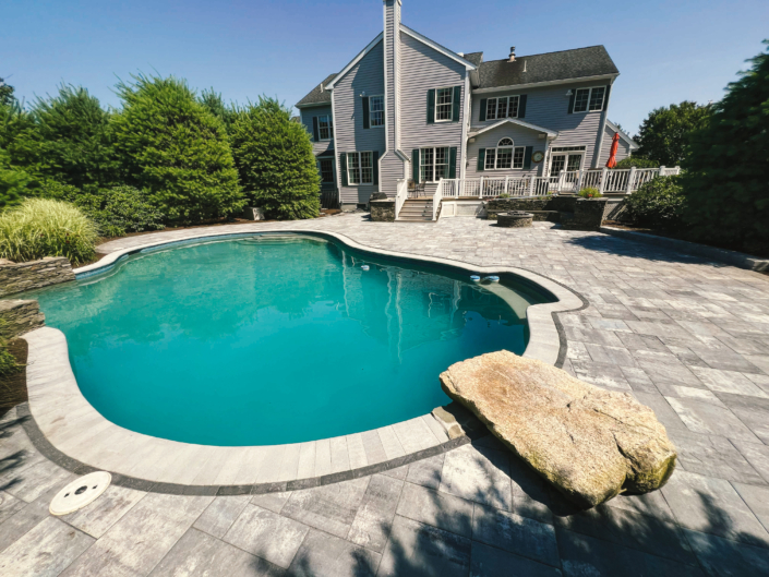 Paver patio surrounding an in-ground swimming pool with natural stone features in the summer.
