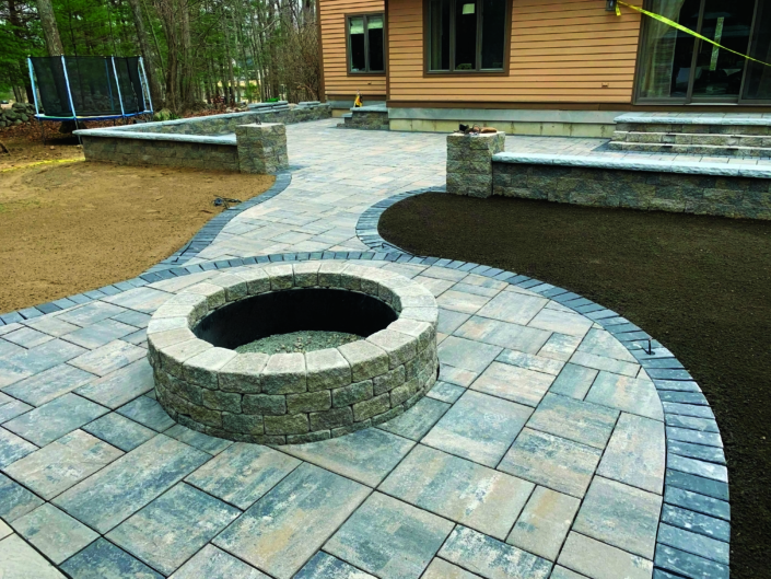 Freshly installed paver patio with a walkway leading to a fire pit.